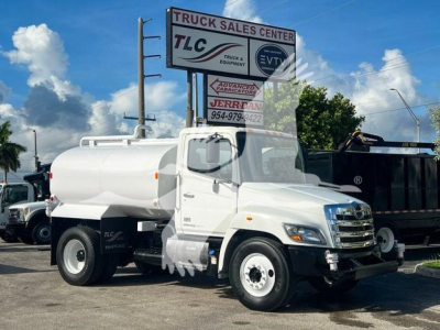 Truck with tank body in front of a dealership sign; visible text on the large sign includes 'TRUCK SALES CENTER' and logos. No other legible labels or specifications on the vehicle are clearly readable in the image.