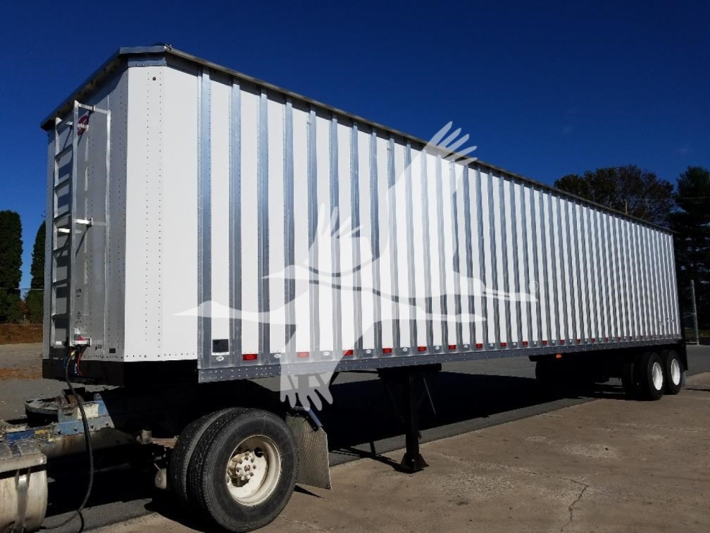 Trailer side view showing a long white open-top trailer with metal panel walls and dual rear axles.