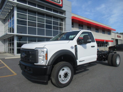 Ford F-450 cab and chassis truck in white, front-left view, dealership building in background, stock tag visible on windshield.