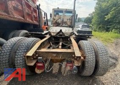 Freightliner FLC112 tractor rear view showing dual rear axles and hitch with plow truck in background.