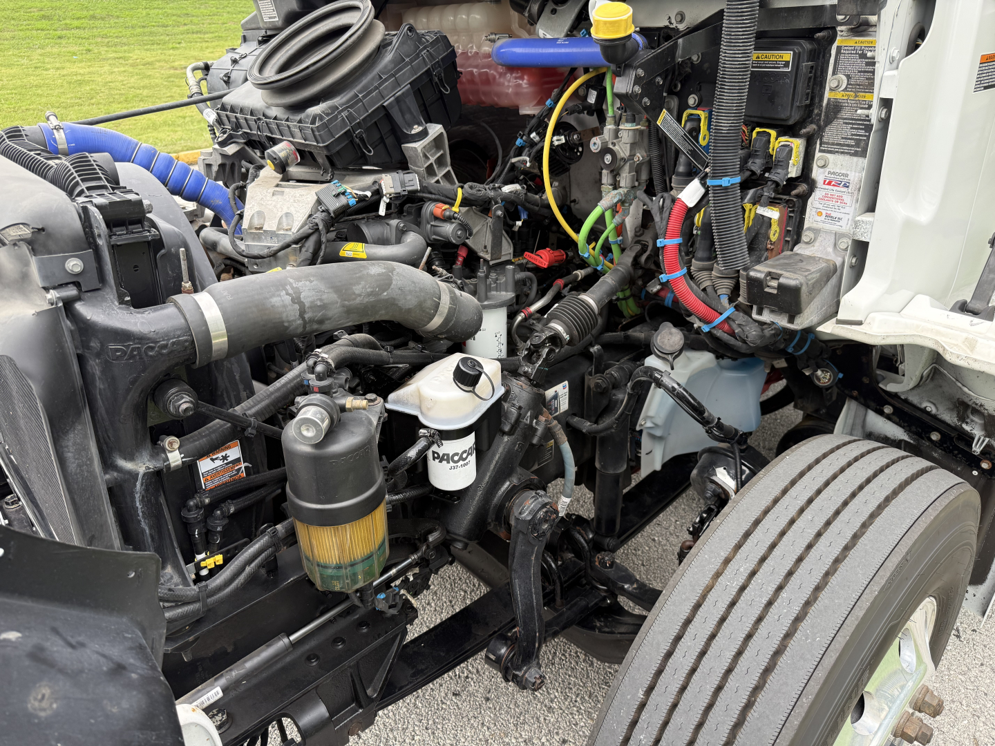 Kenworth T380 engine bay showing coolant reservoir, air intake, hoses, wiring, and various machine components.