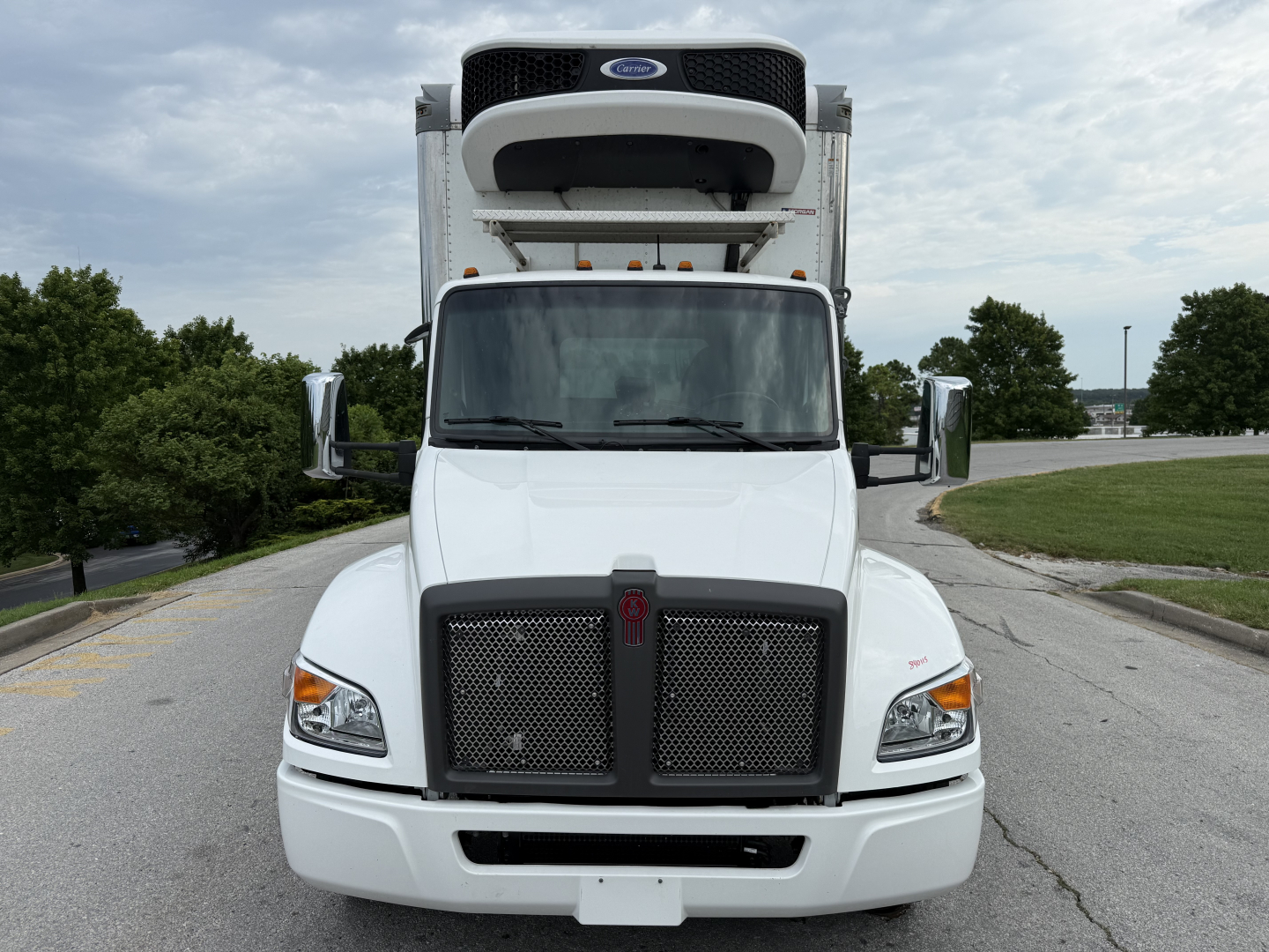 Front view of a white 2023 Kenworth T380 refrigerated truck with a raised refrigerated unit on top, large black grille, rectangular headlights, and side mirrors.