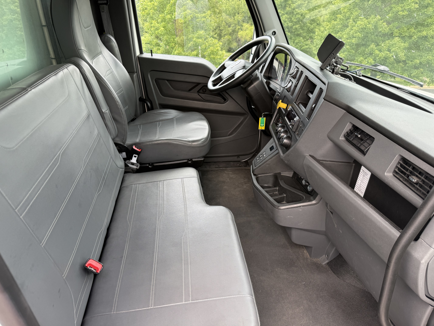 Interior of a Kenworth T380 from the driver’s side, showing a two-person bench seat, steering wheel, dashboard, and center console.