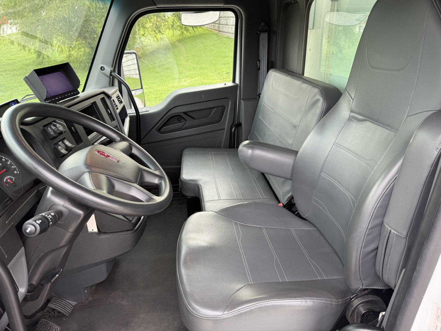 Kenworth T380 interior cab view showing driver's seat and passenger seat, steering wheel, dashboard, and side door.