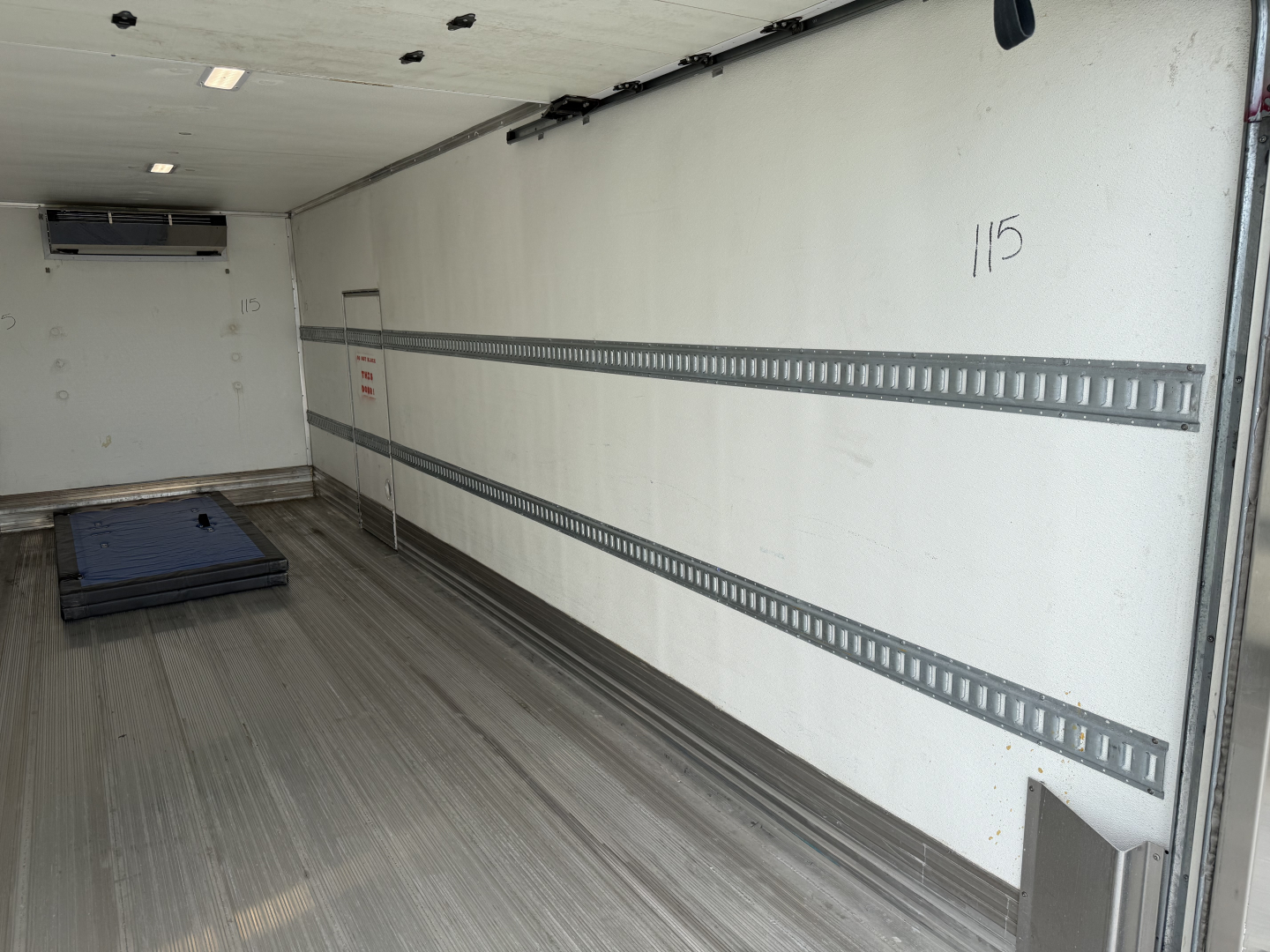 Kenworth T380 refrigerated truck cargo area interior with aluminum floor, sidewall E-track rails, and a pallet on the floor.