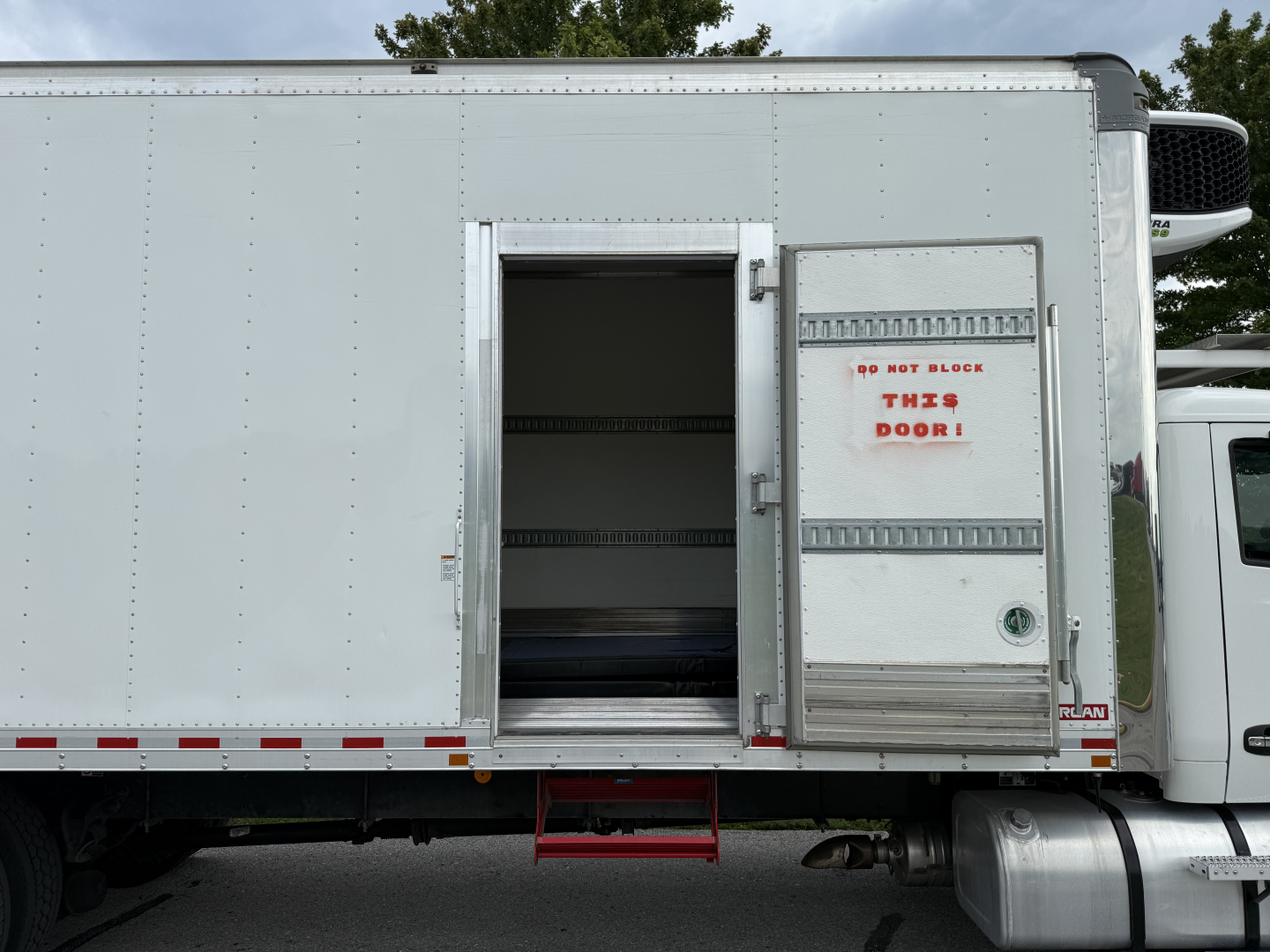 Kenworth T380 refrigerated truck side with open rear access door showing interior shelving and steps.
