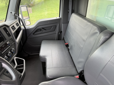 Cab interior of a 2023 Kenworth T380 truck showing driver seat and bench passenger seat with grey upholstery, dashboard controls, and steering wheel.