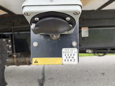 Kenworth T380 refrigeration unit hitch with circular power connector and two warning labels, showing a 230V 60Hz operating plate.