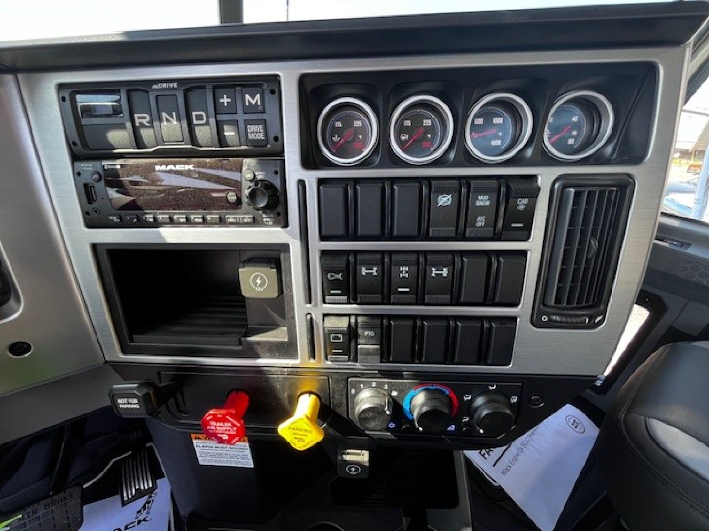 Dashboard of 2026 Mack GR64F showing steering column, gauges, climate controls, gear selector with R N D plus M, and switches.