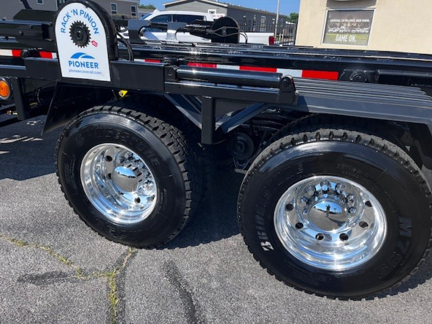 Mack GR64F truck side showing dual rear wheels with chrome rims and black chassis; visible label 'Rack N Pinion' on a sign and tanker/flatbed components.