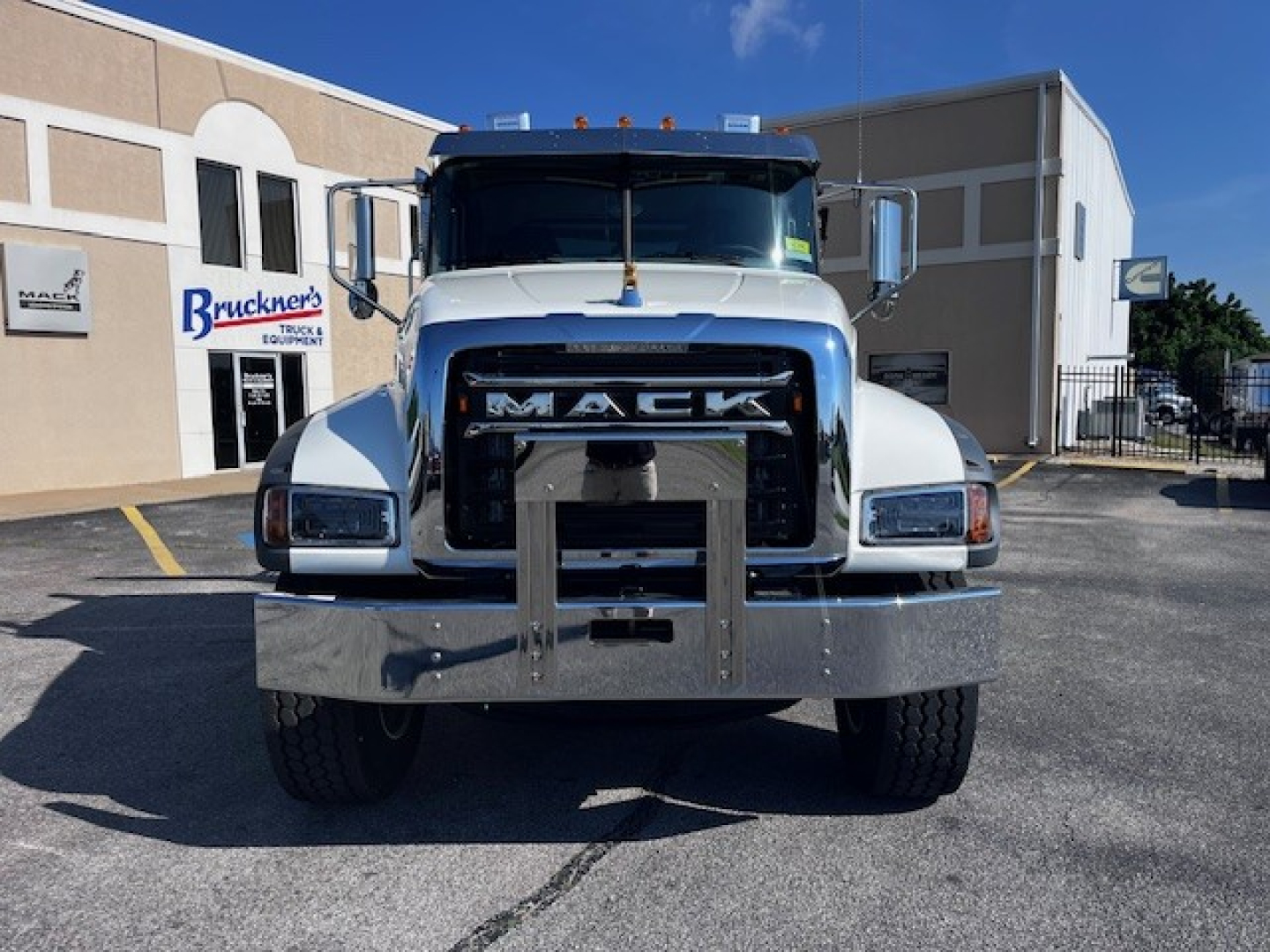 Front view of a white Mack GR64F truck in a dealership lot showing large chrome bumper and grille.