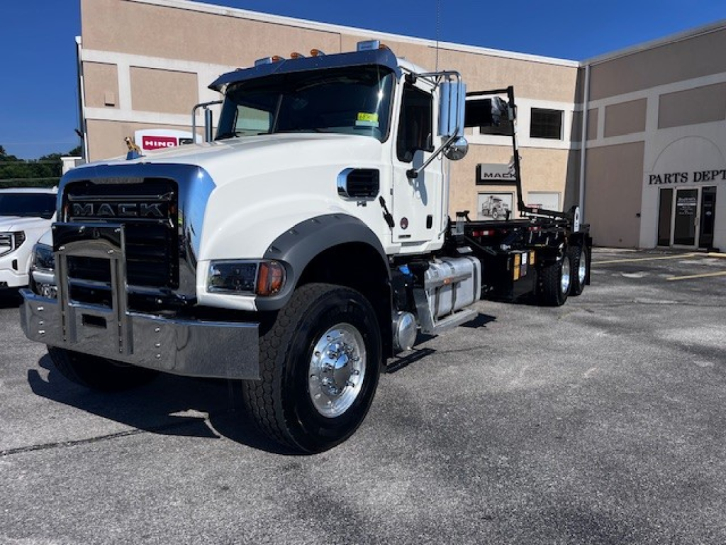 Mack GR64F truck in white with chrome bumper and flatbed/roll-off body, front left view.