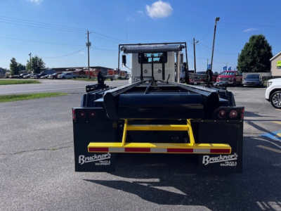 Rear view of a Mack roll-off truck with a black rear frame and yellow bumper; Buckners Equipment logos on mud flaps; red taillights; clear sky.