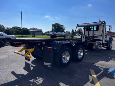 Mack GR64F truck roll-off chassis with extended frame, dual rear axles, and Crew cabin showing bare metal platform and hydraulic components.