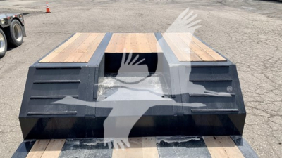 Trailer bed with wooden deck sections and black metal side structures, viewed from rear showing central gap and ramps.