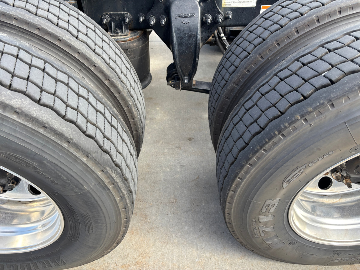 Freightliner truck dual rear axles with tires and bogie suspension showing tread detail and rims.