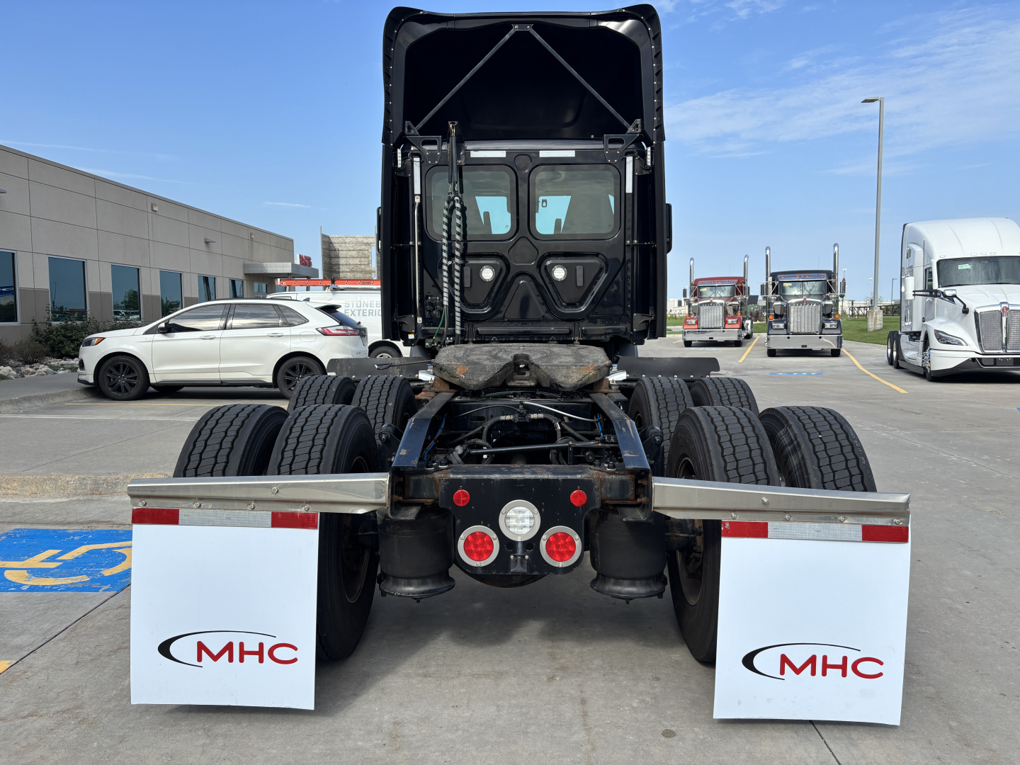 Truck rear view showing fifth wheel and dual rear axles with mud flaps bearing MHC logo and vertical exhaust on cab, no trailer attached.