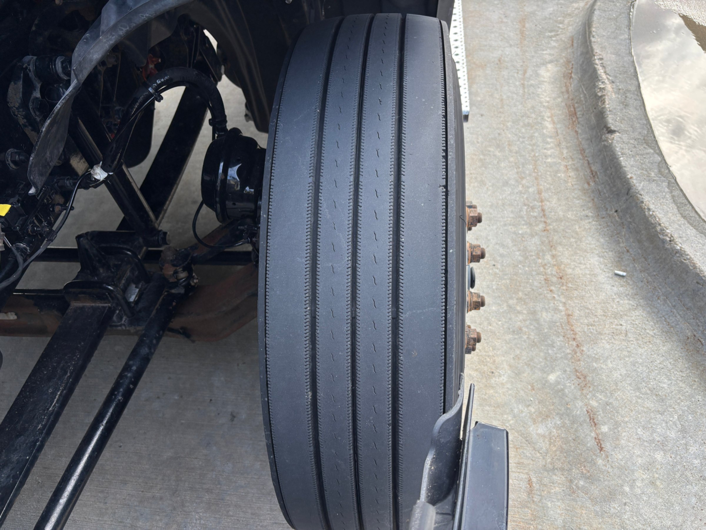 Truck wheel and front suspension detail with large dual outer tire and rim, mechanical components visible in wheel well.