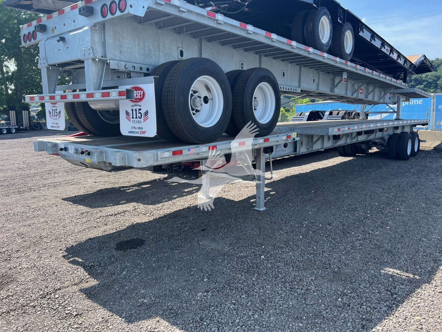 Flatbed trailer with tandem axles and a lowered deck, aluminum frame, and multiple wheels visible; hanging plate with 'VED49030' sticker at rear.