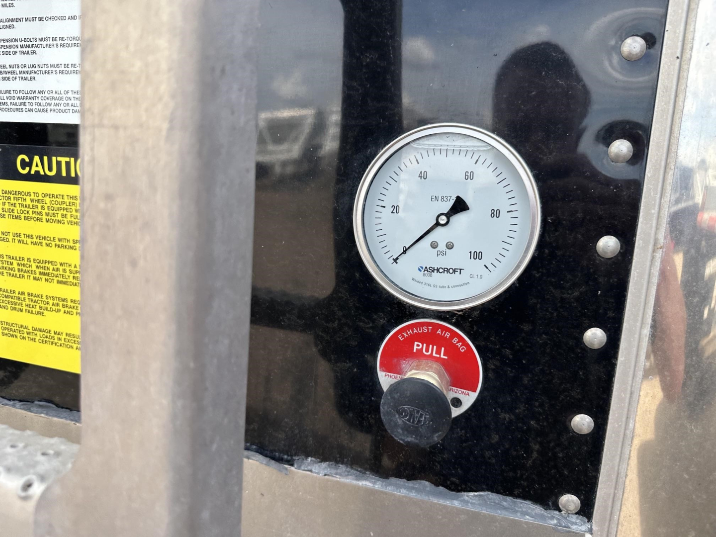 Gauge panel showing a pressure gauge and a red pull handle with a black knob labeled PULL, surrounding metal frame and warning label stickers.