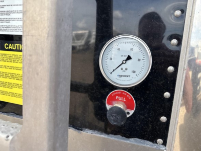 Gauge panel showing pressure gauge and red pull handle on grain trailer exterior.