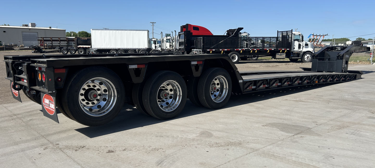 Load King lowboy trailer showing triple-axle configuration with polished aluminum wheels and flatbed deck.
