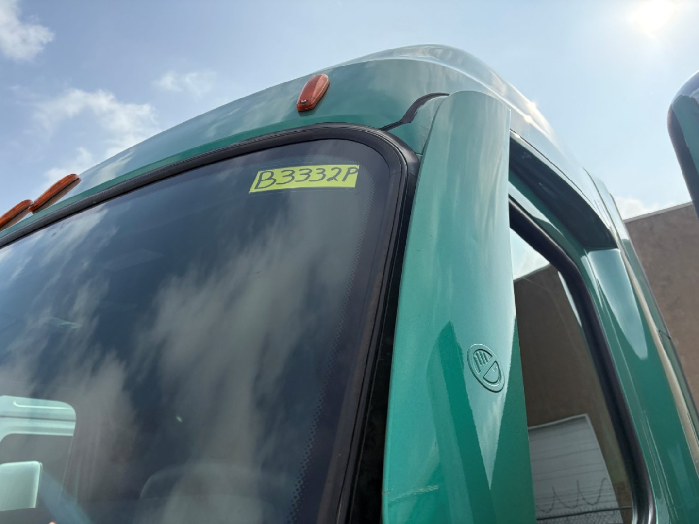 Truck cab front window with yellow stock sticker reading B3332P on a teal Freightliner Cascadia 126 sleeper.