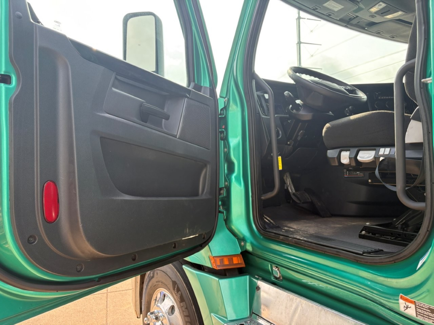 Freightliner Cascadia 126 truck cab interior and open door showing driver seat and dashboard, green exterior, with entry step and door panel.