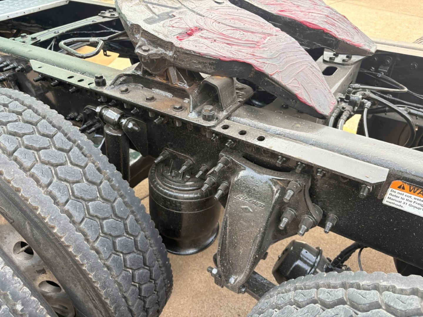 Freightliner Cascadia 126 chassis showing frame, air suspension bag, drive axle area, and damaged cab roof components.