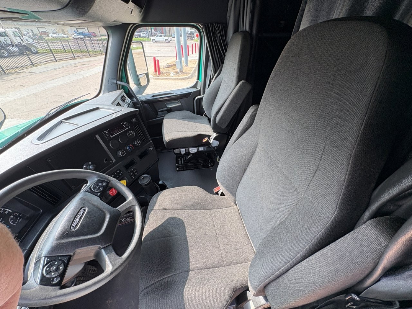 Cab interior of a 2023 Freightliner Cascadia 126, front seats, steering wheel, dashboard with gauges and controls visible.