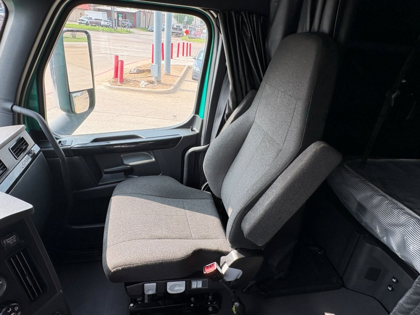 Cab interior of a 2023 Freightliner Cascadia 126 truck showing the driver's seat and a glimpse of the dashboard and sleeper area.