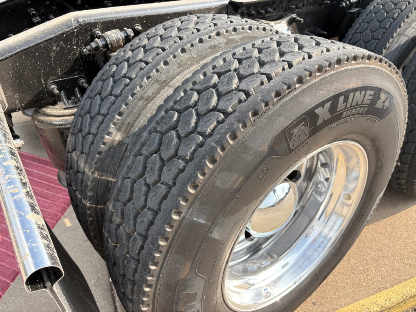 Freightliner Cascadia 126 rear dual rear tires showing XLine tire with rugged tread, chrome hubcap, and suspension components in view.