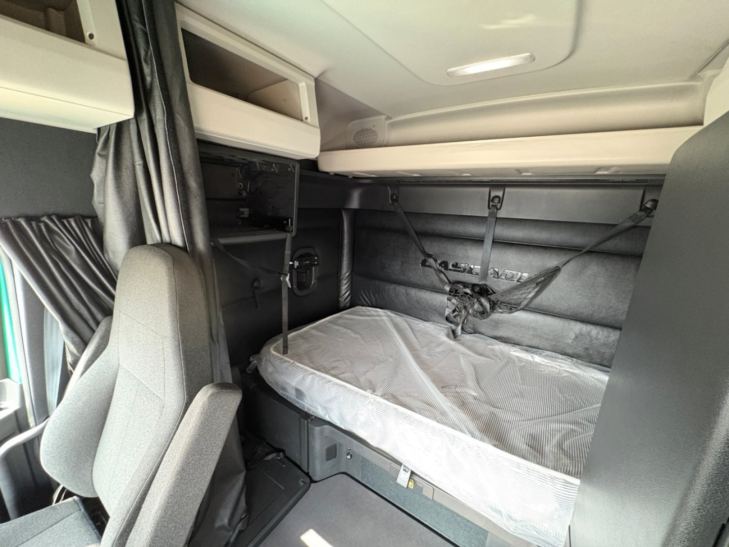 Cab interior of a Freightliner Cascadia 126 sleeper showing bunk bed with protective cover, storage compartments, and cabin walls
