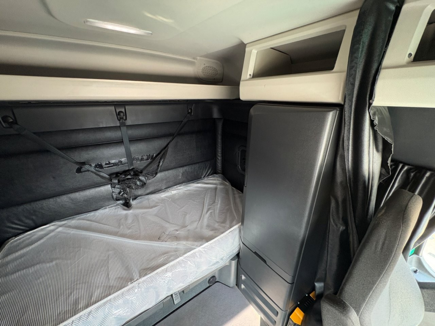 Freightliner Cascadia 126 truck sleeper cab interior showing bunk bed area with mattress, side storage cabinet, and overhead shelf.