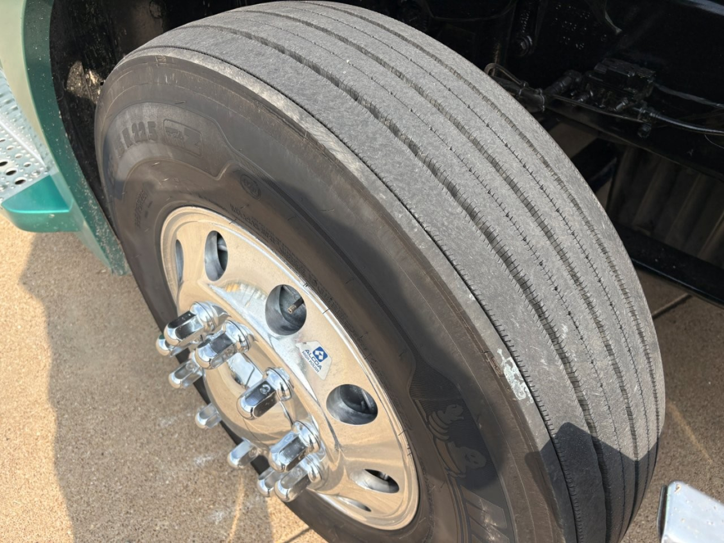 Truck wheel/tire close-up showing front dual-axle aluminum rim with lug nuts on Freightliner Cascadia 126, tread visible.