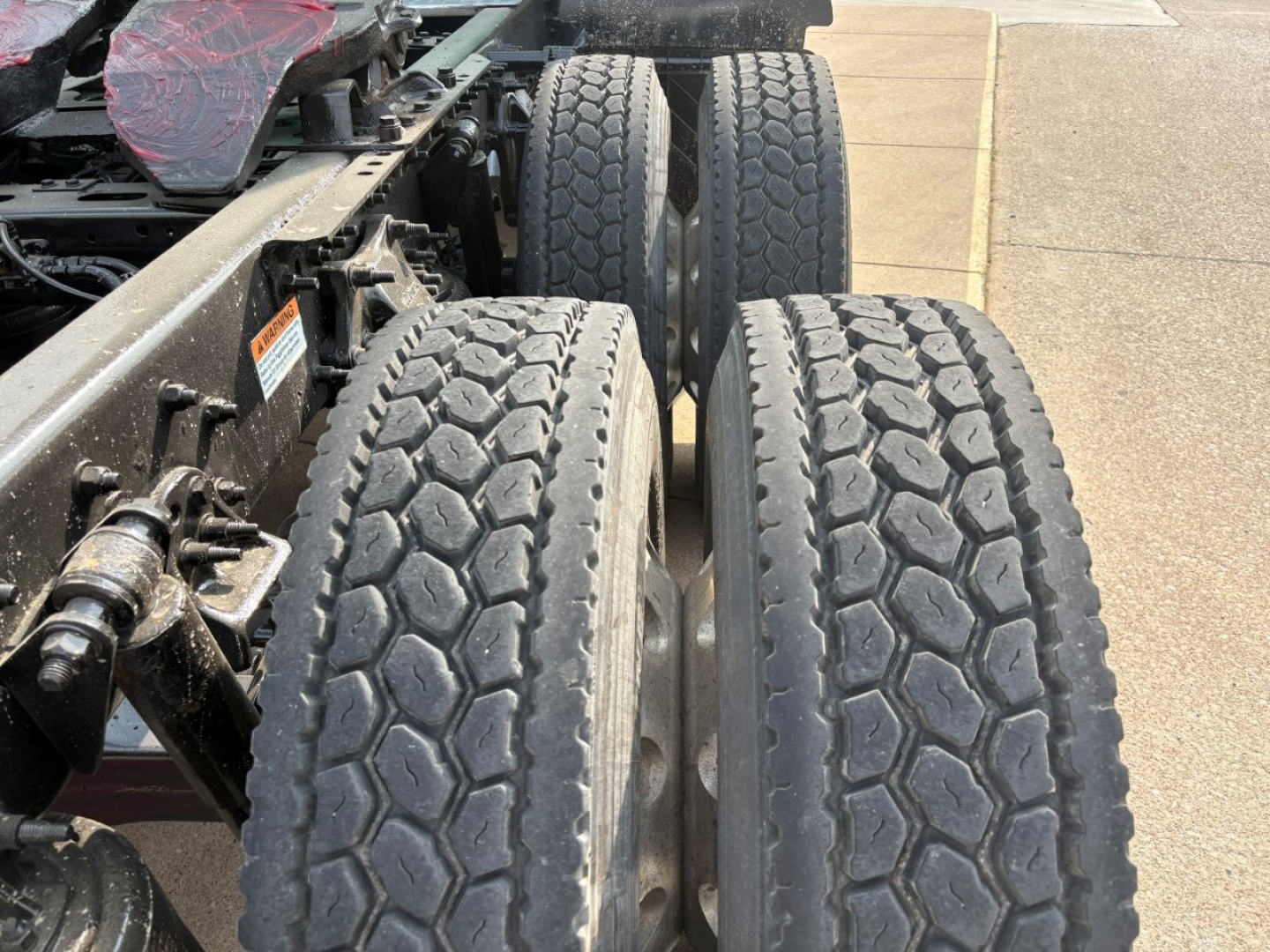 Truck chassis showing dual rear axles with heavy tread tires on a Freightliner Columbia/Cascadia-type frame; visible wheel hubs and suspension components.
