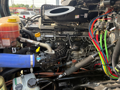 Engine bay of a 2023 Freightliner Cascadia 126 showing various hoses, wiring, coolant reservoir, air intake, and labeled components.