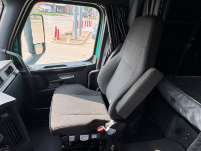 Cab interior of a 2023 Freightliner Cascadia 126 truck showing the driver's seat and a glimpse of the dashboard and sleeper area.