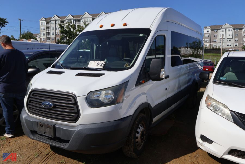 Ford Transit 2016 high-roof passenger van in white, front-left view, showing Ford grille and side mirrors.