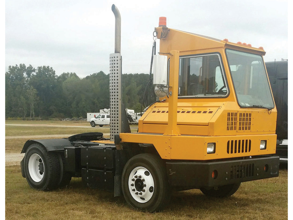 Truck cab of a 2017 Ottawa YT-30 yard truck in service with a tall exhaust stack and orange cab, front view angled to left.
