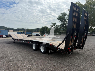 Lowboy trailer with dual ramps raised at rear, long wooden deck, three axles, black frame, and DOT lights along sides.