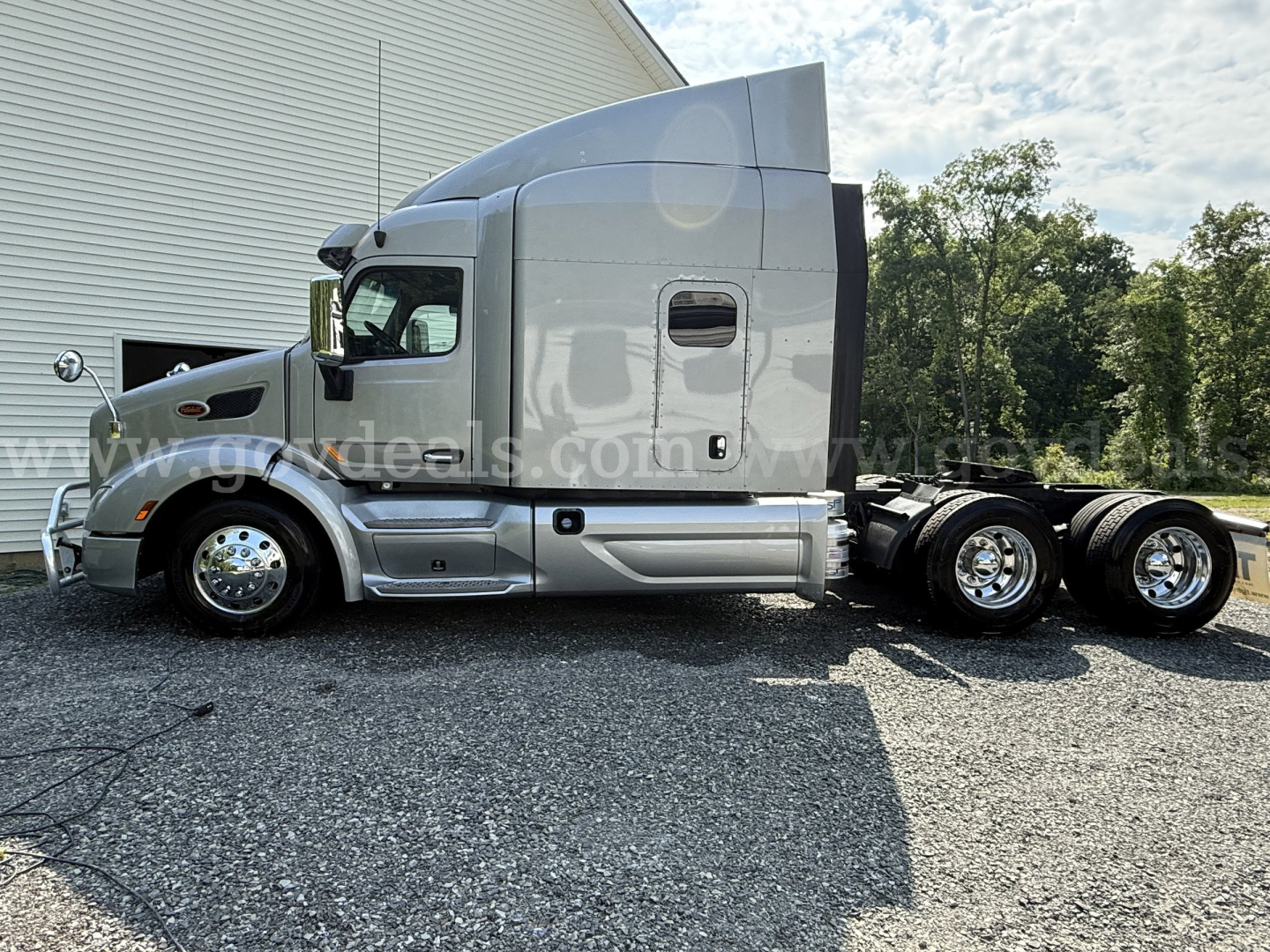 Peterbilt 579 cab with sleeper showing side profile and rear wheels, tag mentions 2019 model, chrome wheels, silver paint, no trailer attached.