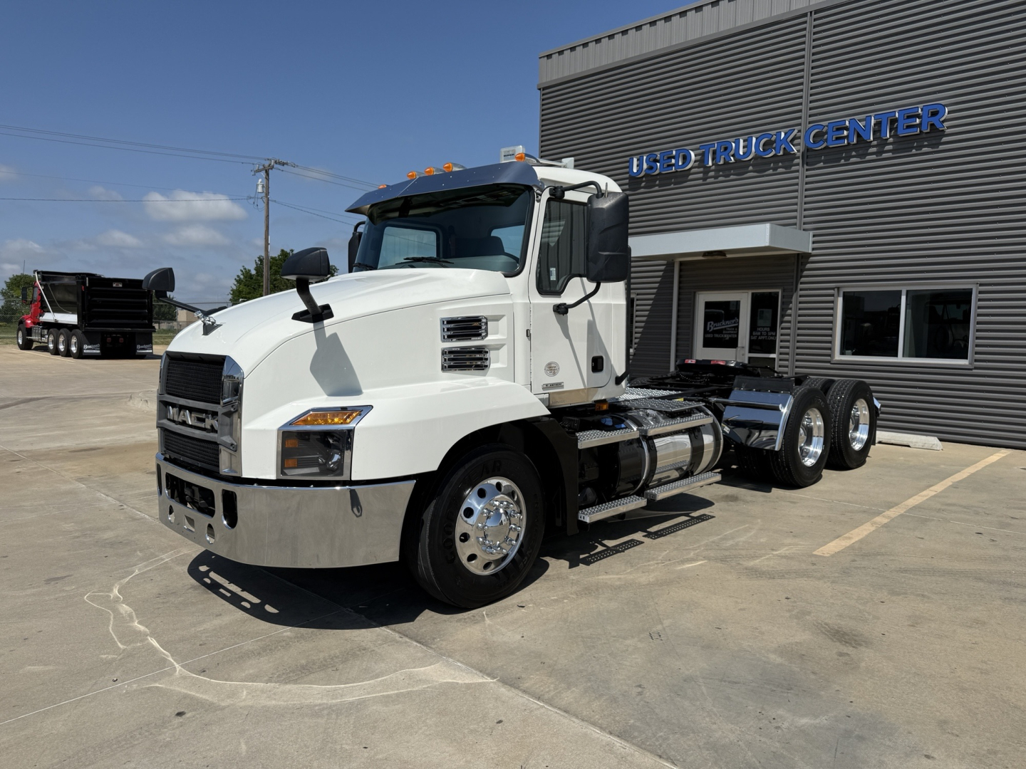 White 2021 Mack AN64T conventional daycab truck shown in parking lot near a used truck center, with 6-wheel configuration and chrome bumper.