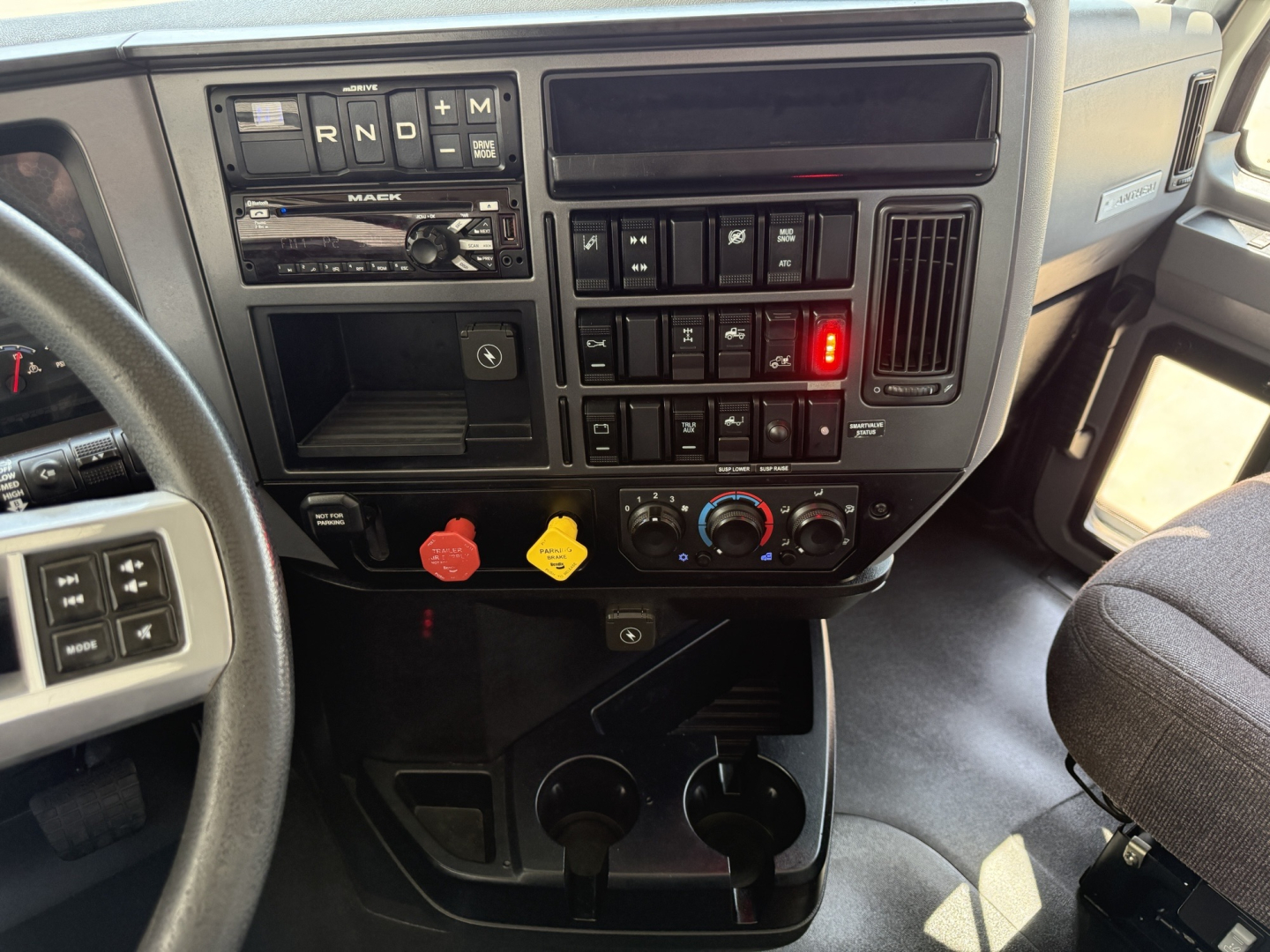 Dashboard of 2021 Mack AN64T daycab showing instrument panel with gear selector PRND and controls, switches, red and yellow warning levers, climate knobs, cup holders.