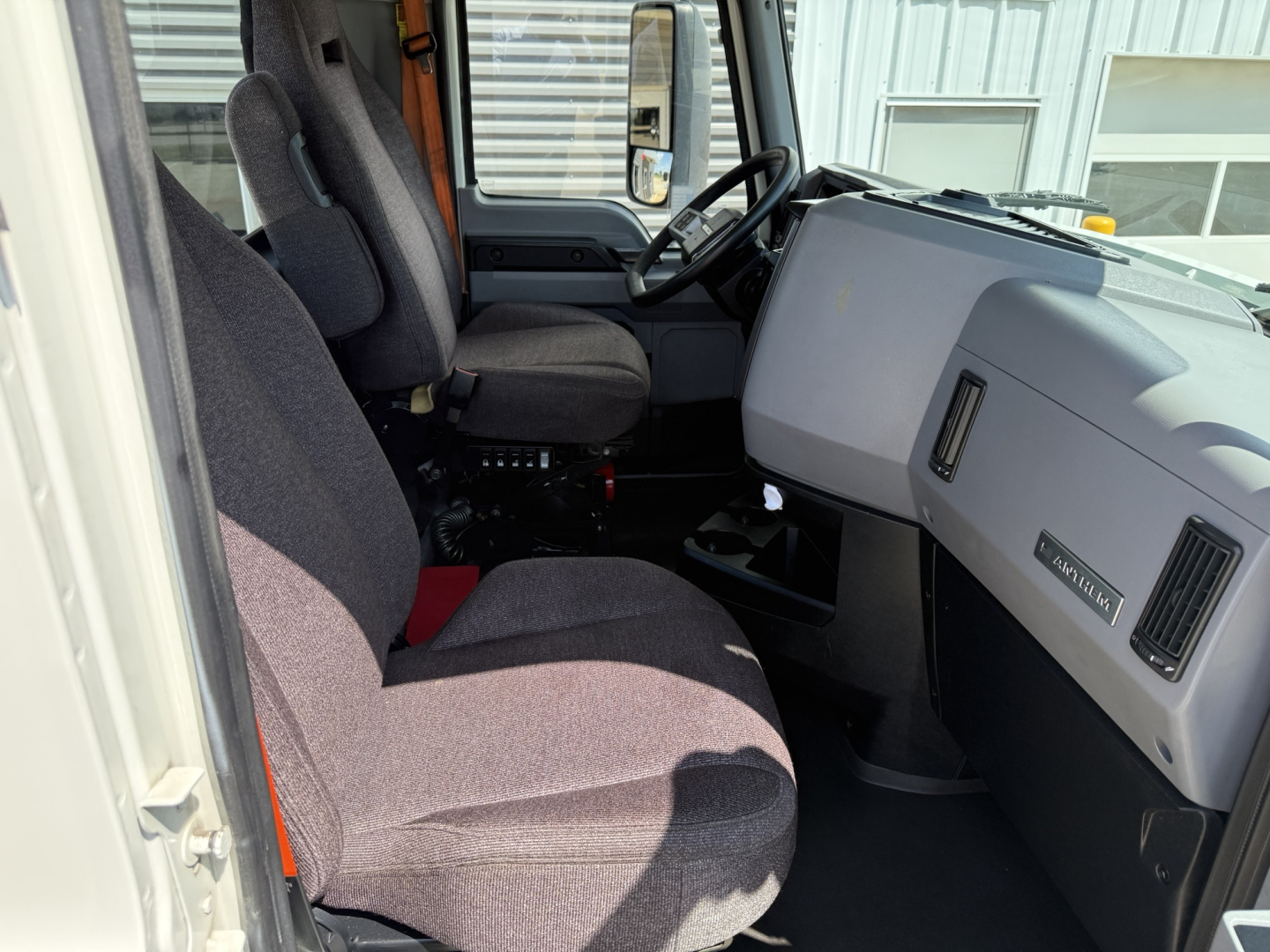 Truck cab interior of a 2021 Mack AN64T showing driver seat, passenger seat, steering wheel, dashboard, and center console with minimal visible controls.