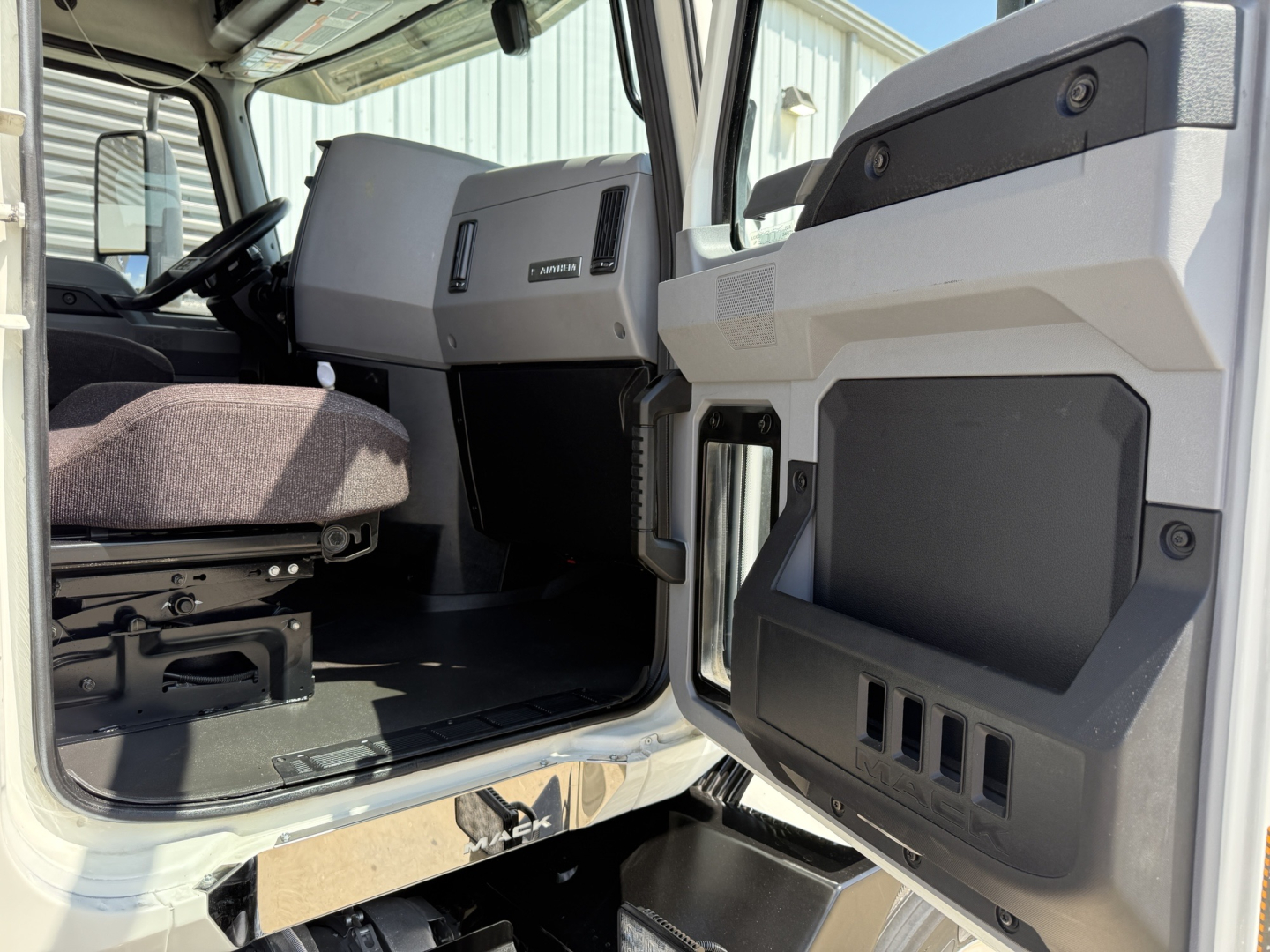 Cab interior of a 2021 Mack AN64T truck showing driver seat, dashboard, and open door with storage panels visible.