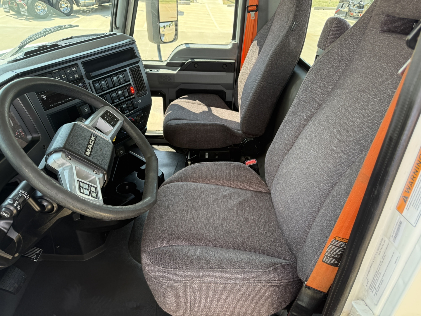 Mack AN64T truck cab interior showing steering wheel with integrated controls, dashboard, and two front seats in gray fabric.
