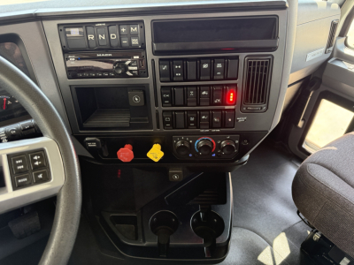 Dashboard of 2021 Mack AN64T daycab showing instrument panel with gear selector PRND and controls, switches, red and yellow warning levers, climate knobs, cup holders.