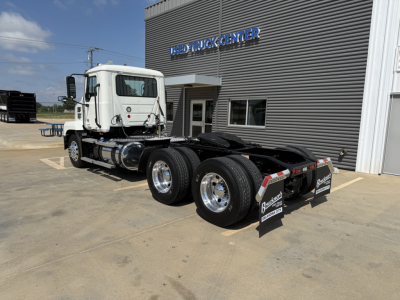 Mack AN64T daycab truck in front of a dealership, side view shows dual rear axles and fifth wheel, white cab, dealership building in background.