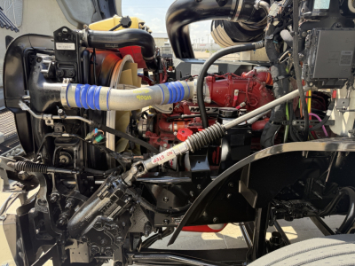 Mack AN64T engine bay showing red engine block, blue hose, and various pipes and components.